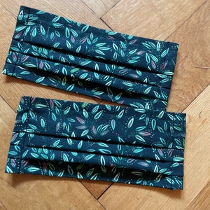 May include: Two black face masks with a green and white leaf pattern. The masks are pleated and have a dark green background.