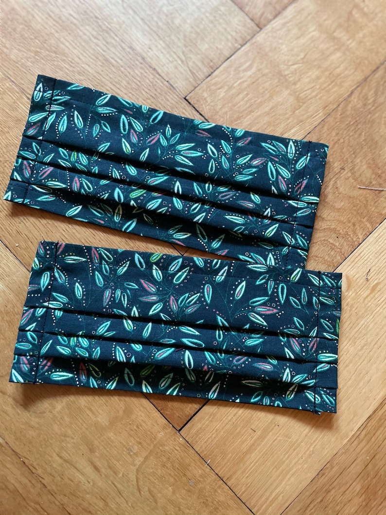 May include: Two black face masks with a green and white leaf pattern. The masks are pleated and have a dark green background.