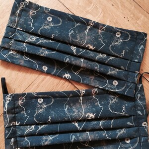 May include: Two dark blue fabric face masks with a white and gold anchor and chain pattern. The masks are pleated and have elastic ear loops.