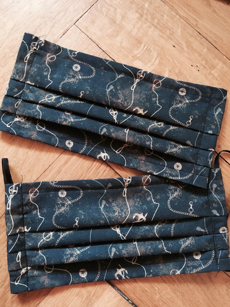 May include: Two dark blue fabric face masks with a white and gold anchor and chain pattern. The masks are pleated and have elastic ear loops.