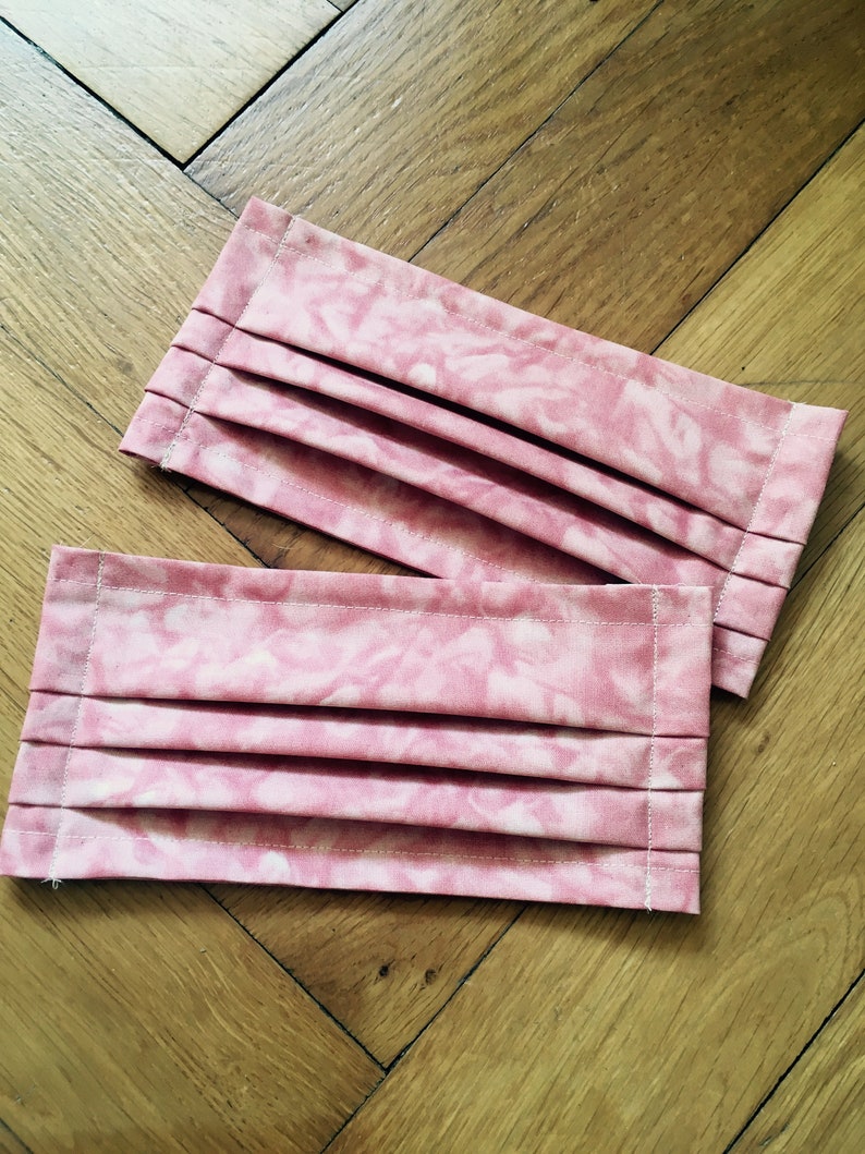 May include: Two pink face masks with a tie-dye pattern. The masks are pleated and have a white background with pink swirls.