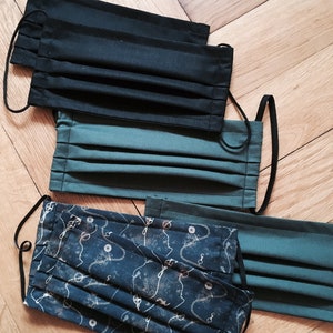 May include: Four face masks, two black, one green, and one with a blue and white pattern. The masks are folded and have elastic ear loops.