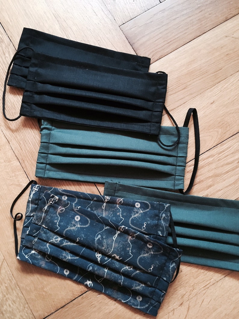 May include: Four face masks, two black, one green, and one with a blue and white pattern. The masks are folded and have elastic ear loops.