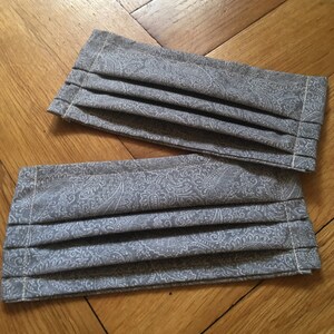 May include: Two gray fabric face masks with a white paisley pattern. The masks are pleated and have a sewn edge.
