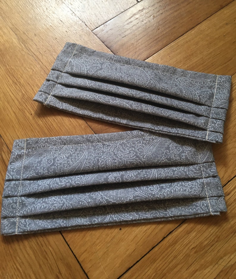 May include: Two gray fabric face masks with a white paisley pattern. The masks are pleated and have a sewn edge.