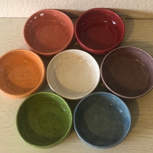 May include: Set of seven speckled ceramic bowls in various colors, including red, orange, green, blue, gray, and white. The bowls are all the same size and shape, and they have a speckled finish.