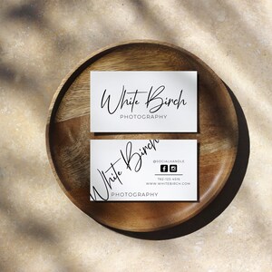 K&ouml;nnte beinhalten: Zwei wei&szlig;e Visitenkarten mit schwarzem Text auf einem Holzteller. Die obere Karte lautet "White Birch Photography". Die untere Karte lautet "White Birch Photography" mit einem Social-Media-Handle, einer Telefonnummer und einer Website-Adresse.
