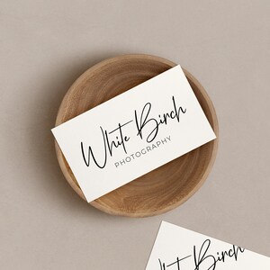 K&ouml;nnte beinhalten: Wei&szlig;e Visitenkarte mit dem Text "White Birch Photography" in handschriftlicher Schrift auf einer Holzoberfl&auml;che.