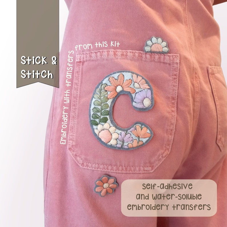 Op de afbeelding: Roze denim overall met een grote geborduurde letter C op de achterzak. De letter is gemaakt van kleurrijke bloemen en bladeren. De tekst "Stick & Stitch" en "Embroidery with transfers from this kit" is zichtbaar aan de linkerkant van de afbeelding. De tekst "self-adhesive and water-soluble embroidery transfers" is zichtbaar aan de rechterkant onderaan de afbeelding.