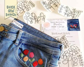 Puede incluir: Un par de pantalones vaqueros azules con un pequeño bolsillo en la parte delantera. El bolsillo tiene un diseño bordado de flores de colores. Junto a los vaqueros hay varias hojas de papel con contornos de flores en blanco y negro. Las hojas de papel tienen el texto "Stick and Stitch Paula Pegar y bordar" y "Stick and Stitch".