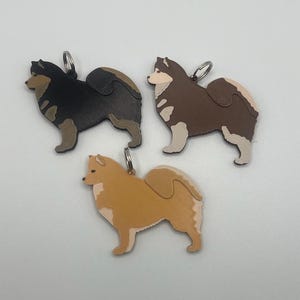 May include: Three dog keychains, each featuring a different color: black, brown, and orange. The keychains are made of leather and have a detailed silhouette of a dog.