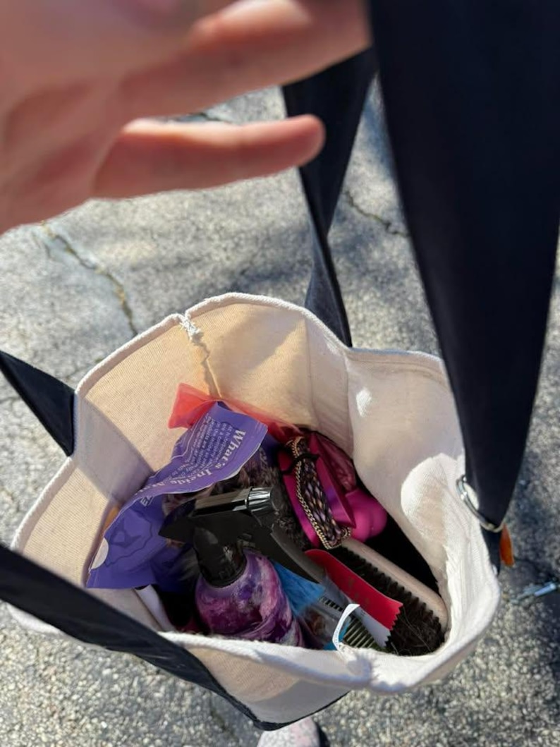 Pode incluir: Uma sacola de lona com al&ccedil;as pretas, cheia de produtos de higiene. A sacola cont&eacute;m um borrifador, escovas, pentes e embalagens. O texto "What's Inside" &eacute; vis&iacute;vel em uma embalagem roxa.