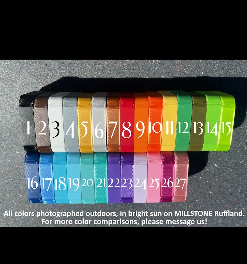 May include: A row of 27 small, square, plastic containers, each painted a different color. The containers are numbered 1 through 27. The colors are photographed outdoors in bright sunlight.