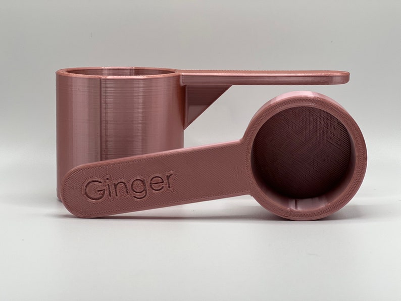 May include: A rose gold colored measuring spoon with a handle that says "Ginger" on it.
