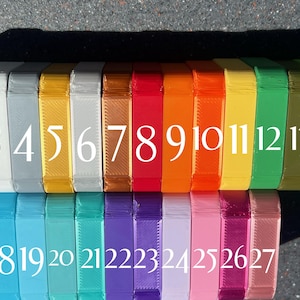 May include: A row of 27 small, rectangular boxes, each a different color. The boxes are numbered 1 through 27. The boxes are arranged in two rows, with the first row containing boxes 1 through 14 and the second row containing boxes 15 through 27.