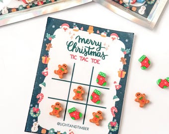 May include: A Christmas-themed tic-tac-toe game with gingerbread men and stocking erasers. The game board is decorated with a festive border and the words "Merry Christmas Tic Tac Toe".