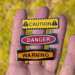 May include: Three black and yellow warning signs with white text. The signs read "Caution", "Danger", and "Warning".