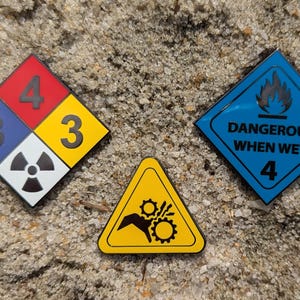 May include: Three safety hazard warning signs. A blue diamond sign with a flame and the text "Dangerous When Wet 4". A yellow triangle sign with a hand and gears. A diamond sign with four quadrants, red, yellow, blue, and white, with the numbers 4, 3, 3, and a radiation symbol.