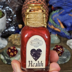 May include: A small, clear glass bottle filled with a shimmering red liquid. The bottle has a cork stopper sealed with gold wax and twine. A label on the front reads "Tortoise Ware's" and features a heart with the word "Health" below.