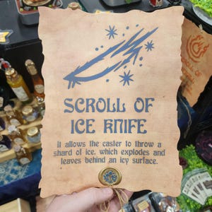 May include: A parchment scroll with the text "SCROLL OF ICE KNIFE" in blue, featuring a blue ice-themed illustration. The scroll's description details its magical properties. A wax seal is attached.