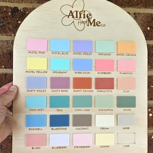May include: Wooden color palette with 25 pastel color swatches, including pink, blue, violet, and orange. The top of the palette has the text "Alfie And Me co" in a floral design. The color names are printed below each swatch.