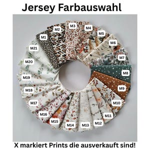May include: A circular arrangement of folded jersey fabric swatches, each labeled with codes M1 through M21. The collection features various patterns including leopard print, floral designs, and polka dots in diverse colors. Text reads Jersey Farbauswahl and X markiert Prints die ausverkauft sind.