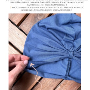 May include: A blue fabric head covering with a knotted front detail and raw, unhemmed edges. The text at the top reads WICHTIGER HINWEIS, followed by German text explaining the manual cutting process and edge rolling, with EINLAGIG-> NAHTLOSE SEITENKANTEN NICHT GES&Auml;UMT! at the bottom.