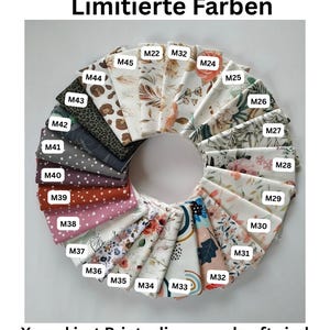 May include: A circular arrangement of folded fabric swatches featuring various patterns including floral, polka dot, leopard print, and abstract designs. Each swatch is labeled with a white tag numbered M22 through M45. The text reads Limitierte Farben and X markiert Prints die ausverkauft sind.