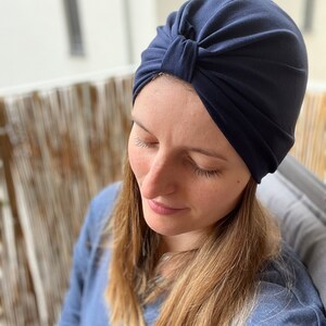 May include: A solid navy blue turban-style head covering featuring a gathered knot detail at the center front. The fabric is smooth and opaque, designed to fit snugly around the head with soft pleats radiating from the central knot feature.
