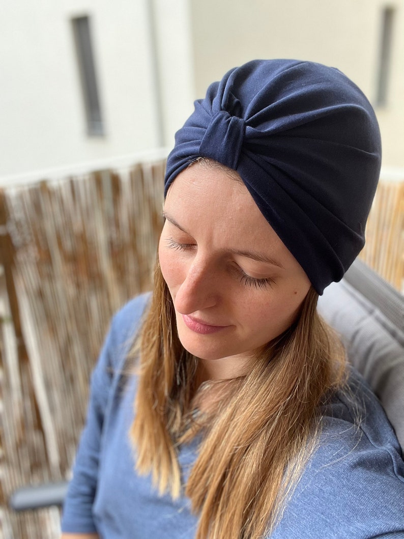 May include: A solid navy blue turban-style head covering featuring a gathered knot detail at the center front. The fabric is smooth and opaque, designed to fit snugly around the head with soft pleats radiating from the central knot feature.