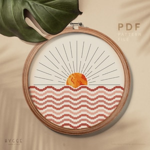 Puede incluir: Un patrón de punto de cruz que presenta una puesta de sol estilizada sobre un océano ondulado. El sol es naranja y amarillo, las olas son rosadas y rojas, y el fondo es blanco. El patrón está en un aro de bordado de madera. El texto "PDF PATTERN FILE" está en la esquina superior derecha de la imagen. El texto "HYGGE CROSS STITCH" está en la esquina inferior izquierda de la imagen.