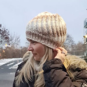 Puede incluir: Un gorro de punto beige y marrón con un ajuste holgado. El gorro está hecho con un patrón de punto texturizado.