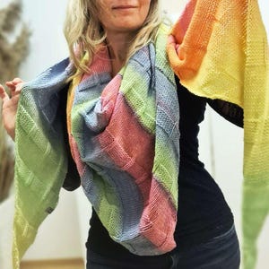 Könnte beinhalten: Ein farbenfroher, handgestrickter Schal in Regenbogenfarben, darunter Rosa, Blau, Grün, Gelb und Orange. Der Schal hat ein strukturiertes, geometrisches Muster. Dieses Accessoire ist perfekt, um jedem Outfit einen Farbtupfer zu verleihen.