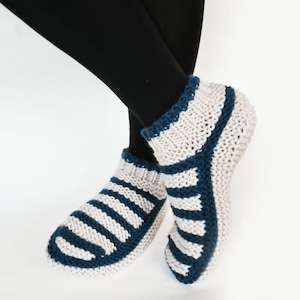 Könnte beinhalten: Ein Paar gestrickte Hausschuhe. Die Socken sind hellgrau mit marineblauen Streifen und Zierleisten. Die Socken sind für den Innenbereich konzipiert und bieten Wärme und Komfort.