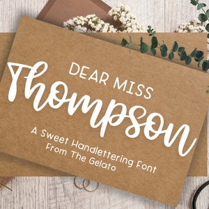 May include: A brown card with white text that reads "Dear Miss Thompson, A Sweet Handlettering Font From The Gelato".