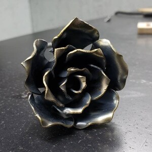 May include: A metal rose sculpture with a dark blue and gold finish. The rose is made of individual petals that are welded together.