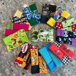 May include: A collection of 12 handmade tissue box covers featuring various designs and patterns. The covers are made from fabric and feature a variety of colors, including green, blue, red, yellow, black, and white. Some of the designs include avocados, chili peppers, and cartoon characters.