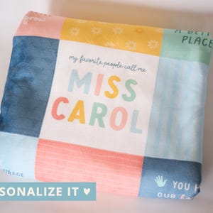 May include: A white and blue patchwork fabric with the text "my favorite people call me MISS CAROL" in colorful letters. The fabric has a yellow, pink, and blue pattern.