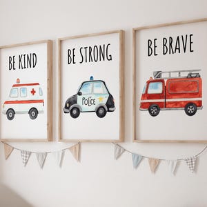 May include: Three framed wall art prints featuring watercolor illustrations of emergency vehicles. The first shows an ambulance with the text BE KIND, the second a police car with BE STRONG, and the third a fire truck with the text BE BRAVE.