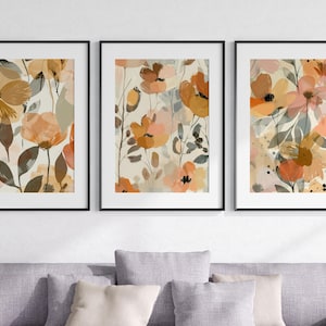 May include: Three framed prints featuring abstract floral designs in shades of orange, brown, and white. The prints are arranged in a row on a white wall.