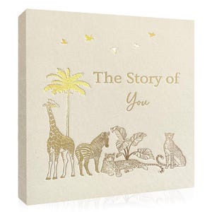 May include: A square, cream-coloured canvas featuring gold foil illustrations of a giraffe, zebra, leopard, palm tree, and birds. The text "The Story of You" is in gold foil.