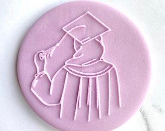 May include: A light purple round cookie with a white outline of a person wearing a graduation cap and gown.