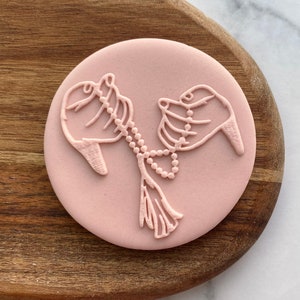 May include: A pink silicone mold with a design of two hands holding a string of beads.