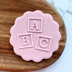May include: Pink fondant cookie with a design of three alphabet blocks, spelling "ABC", in white.