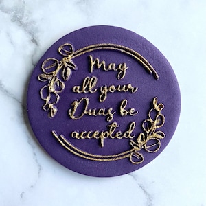 Op de afbeelding: Ronde paarse taarttopper met gouden belettering met de tekst "May all your Duas be accepted" omringd door een gouden bloemmotief.