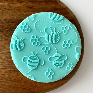 May include: A light blue silicone stamp with a honeycomb and bee design. The stamp features multiple bees with striped bodies and honeycombs.