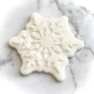 May include: White snowflake-shaped fondant decoration for cakes or cupcakes. The snowflake has a detailed design with a raised texture.