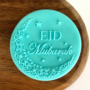 May include: A turquoise blue round silicone stamp with a crescent moon design and the words "Eid Mubarak" in white.