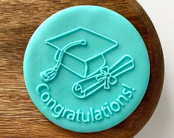 May include: A turquoise blue silicone stamp with a graduation cap and diploma design. The text "Congratulations!" is printed around the edge of the stamp.