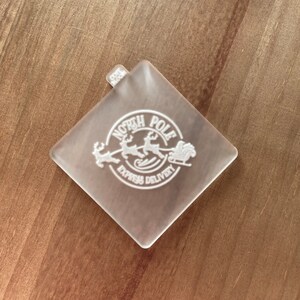 May include: A clear plastic square stamp with a white design of a sleigh pulled by reindeer with the text "North Pole Express Delivery".